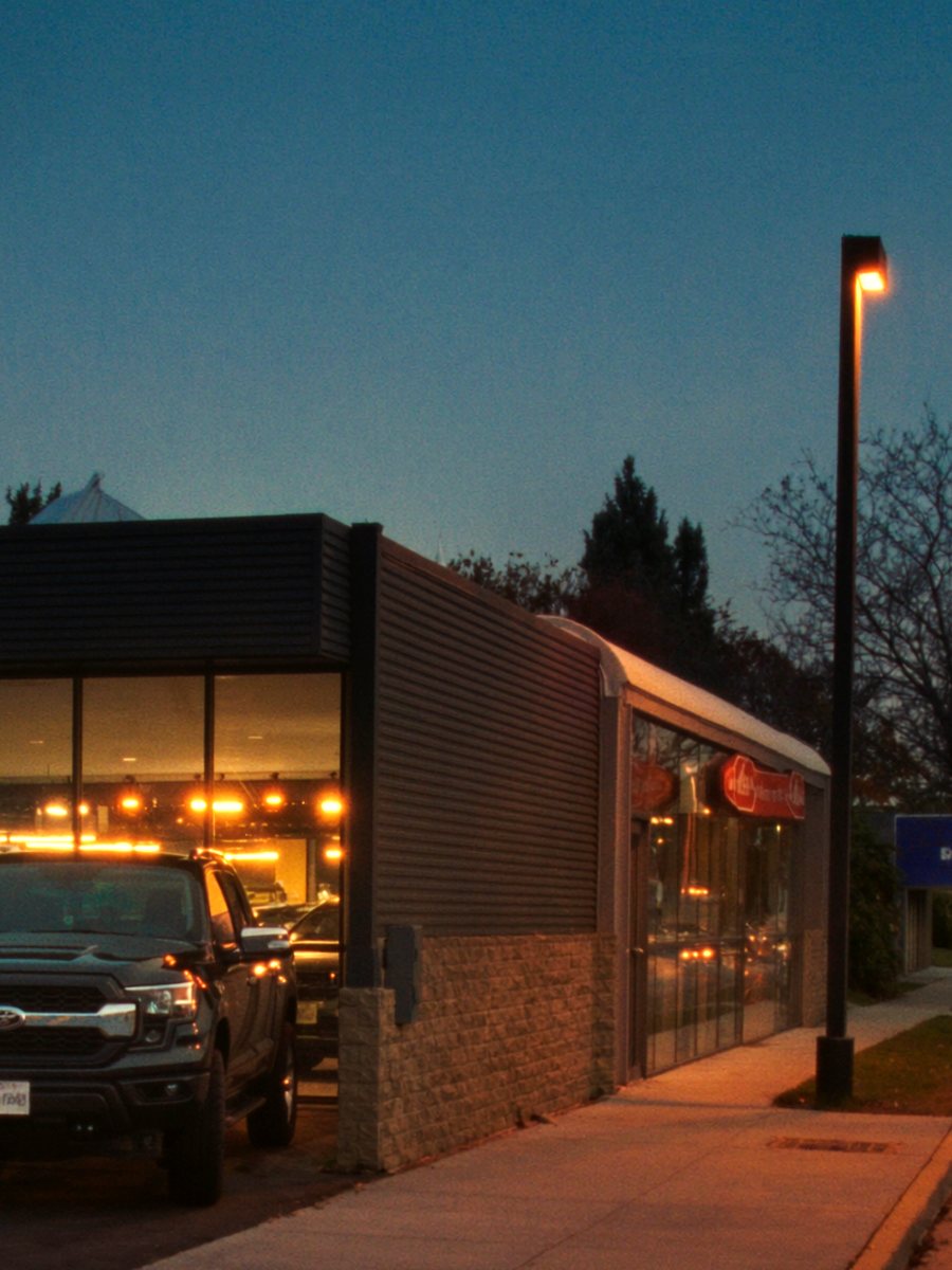 The lit glass front of a dealership showroom at dusk, a new crew cab pickup parked outside.