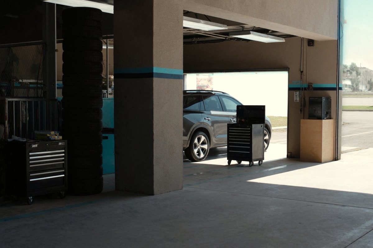 A dealership service drive seen from inside, stacked tyres and a rolling tool cabinet, a new SUV through the open door.